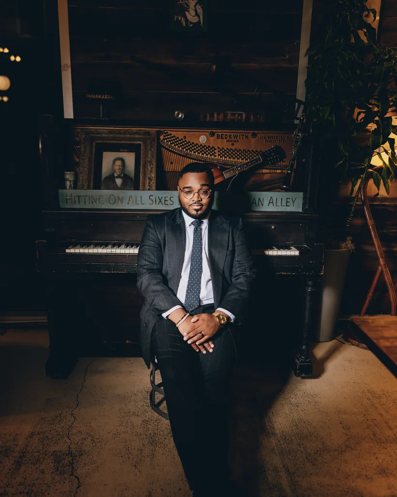 Eugene B. Lee-Johnson seated at a vintage upright piano in a pinstripe suit