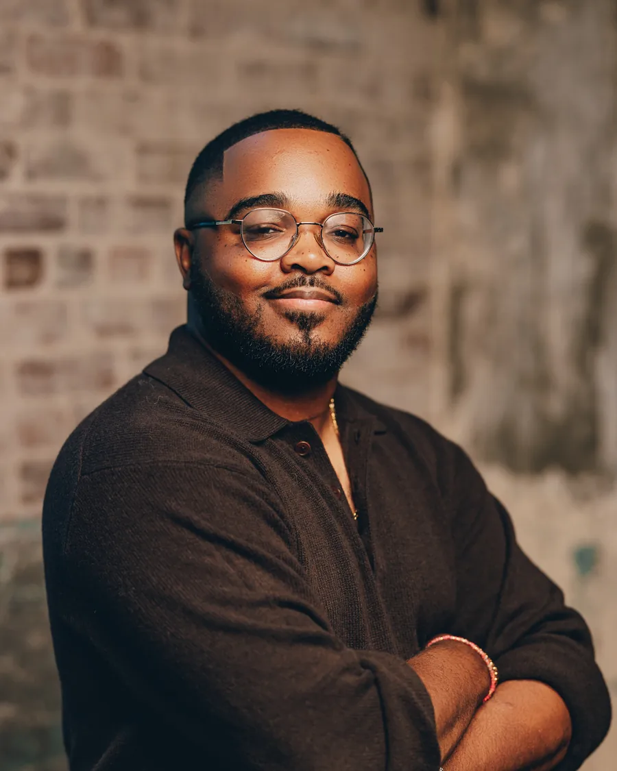 Dr. Eugene B. Lee-Johnson, arms crossed, in a brown sweater against a brick wall